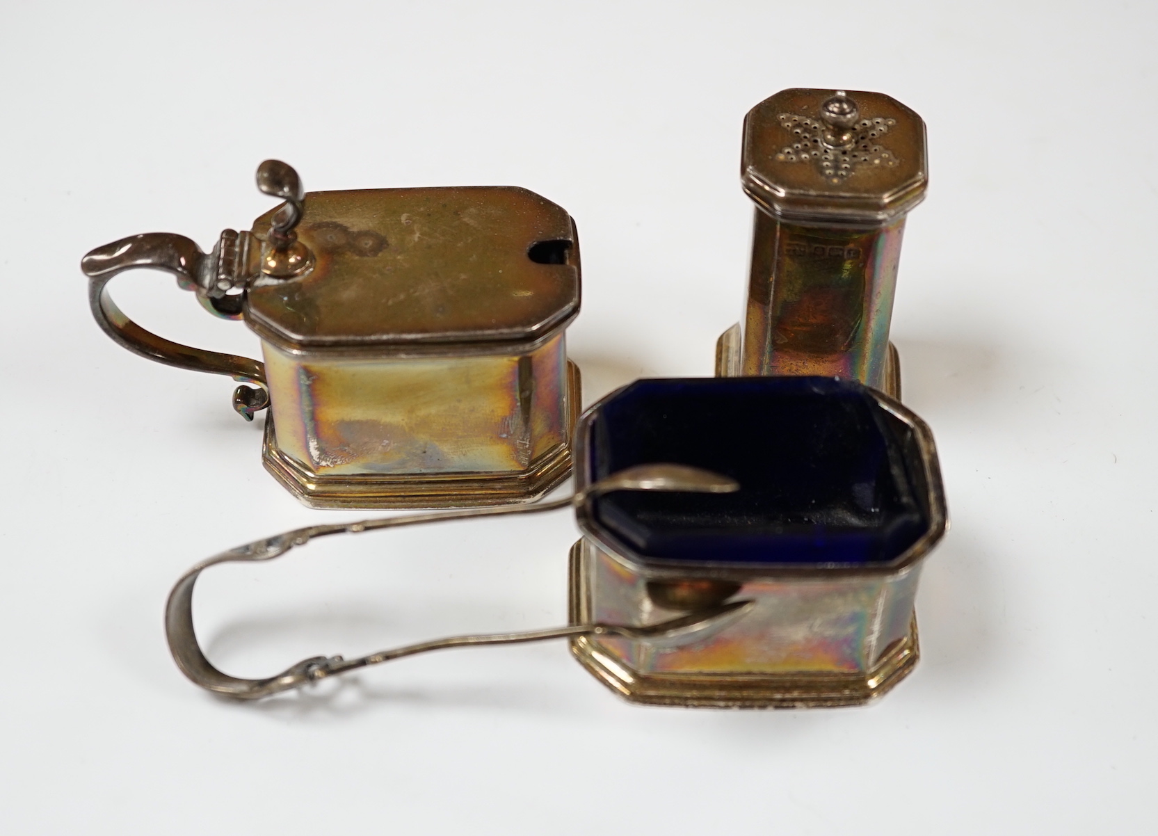 A George V silver three piece condiment set by S.W. Smith & Co, Birmingham, 1917/8/9 and a pair of silver tongs.